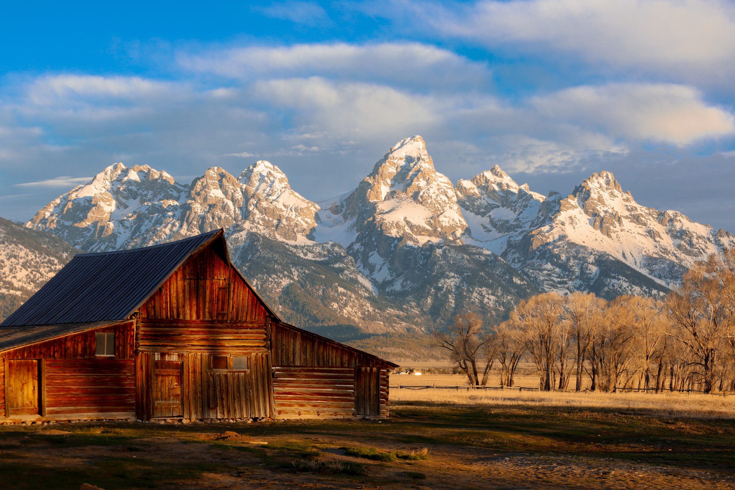 A weathered log barn at dawn beneath snow-covered peaks